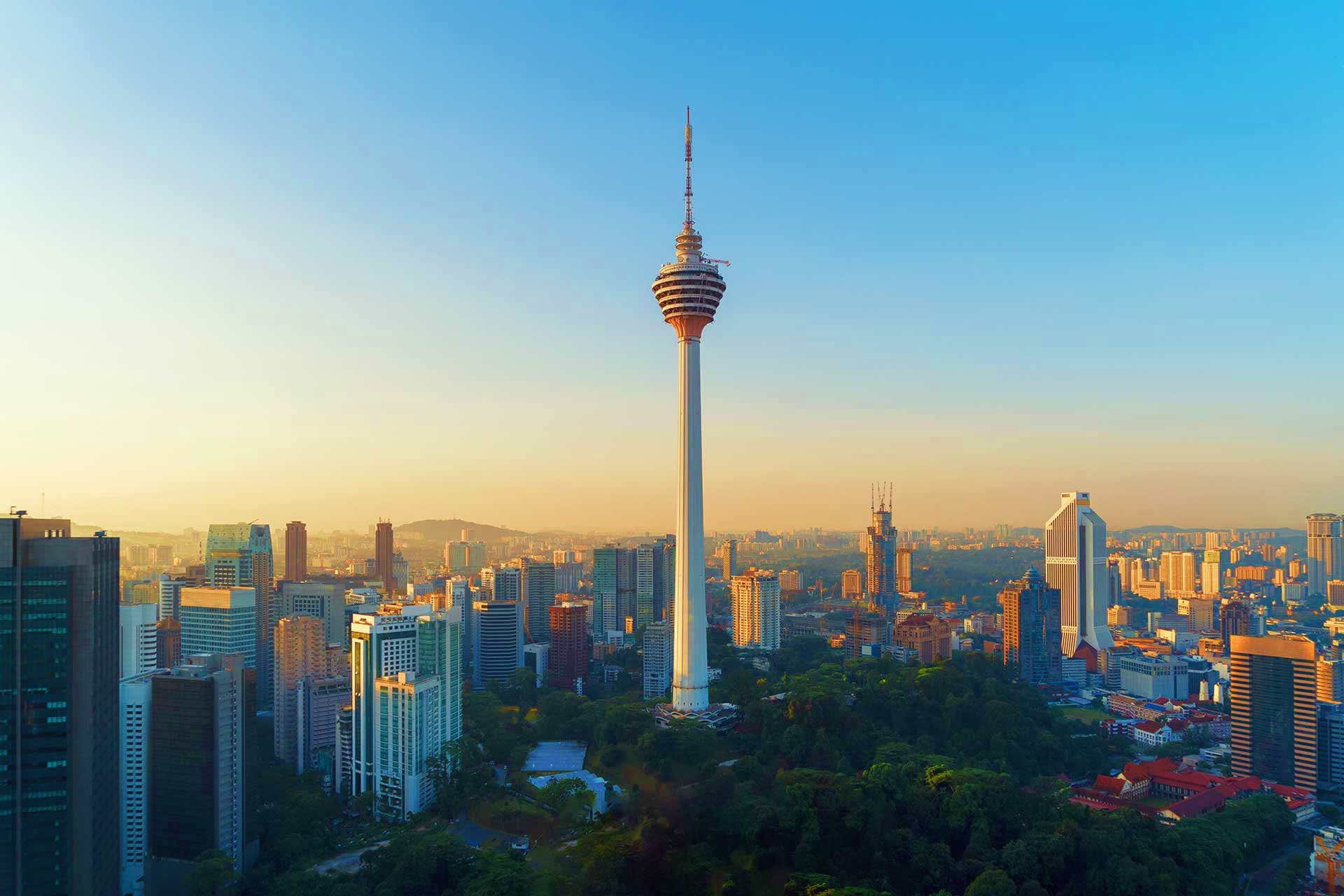 Malaysia Visa Kuala Lumpur skyline at sunset featuring Menara Tower surrounded by high-rise buildings and green vegetation